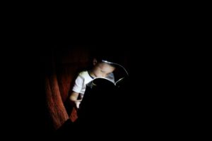 boy reading a book in pajamas at bedtime with a book light